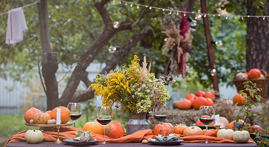 Table full of fall decor: pumpkins, wine glasses, flowers, and candles