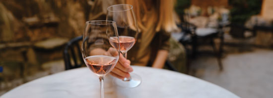 Person's hand reaching for one of two glasses of rosé wine on a dining table