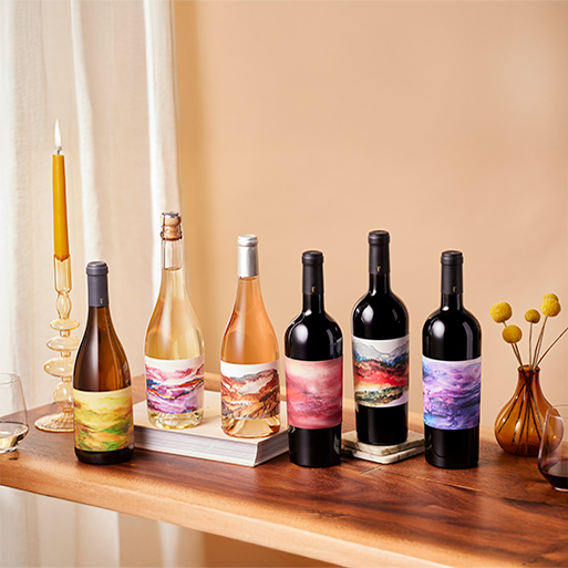 Six bottles of Foley Sonoma wine on a table with a candle, book, and small vase of flowers