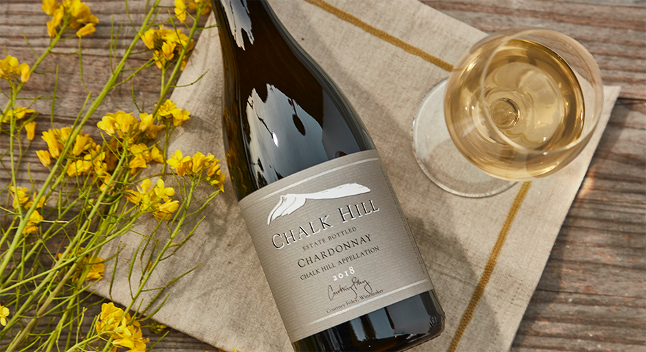A bottle of chalk hill wine laying on a table next to a glass of white wine and yellow flowers