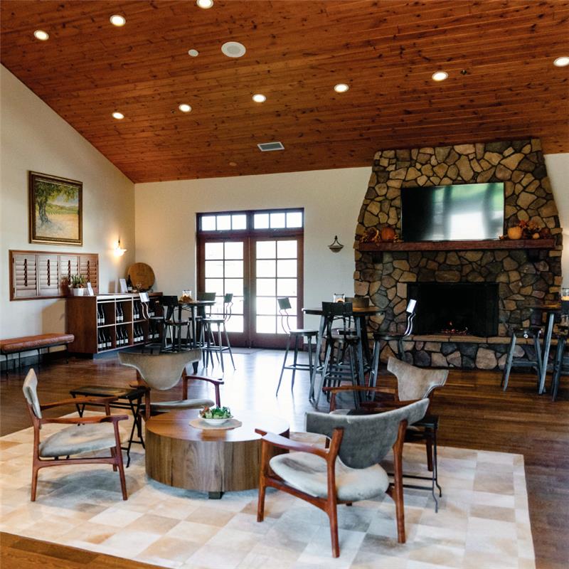 Foley Estates tasting room with multiple sitting areas, a cozy fireplace, vaulted wood ceilings, wood floors, soft sunlight, and a photo on the wall.