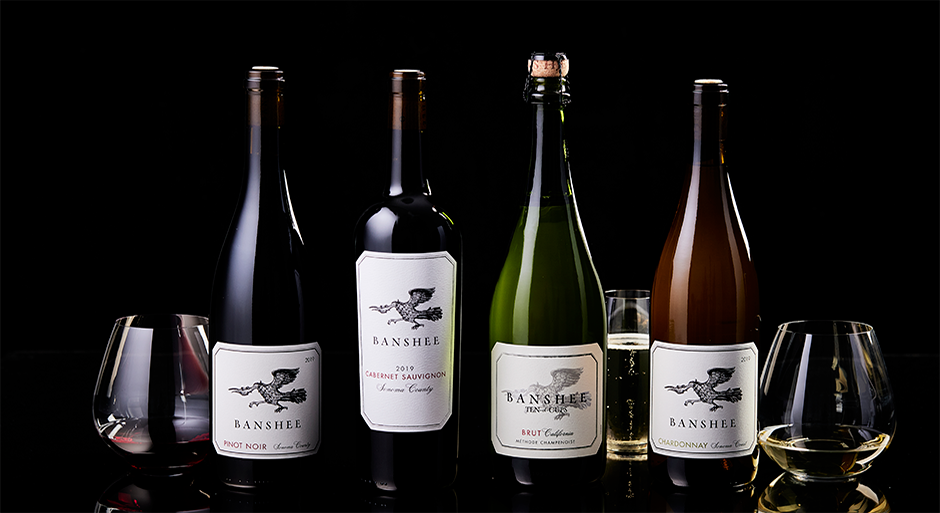 4 bottles of banshee wines with a few glasses with wine in them on a dark background
