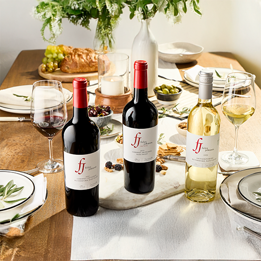 Foley Johnson red and white wines on a wooden table with plated food, flowers, and white table settings