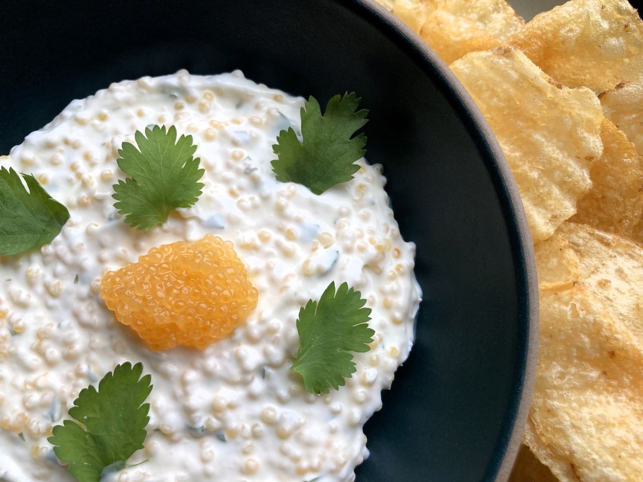 Bowl of dip topped with caviar and a side of potato chips