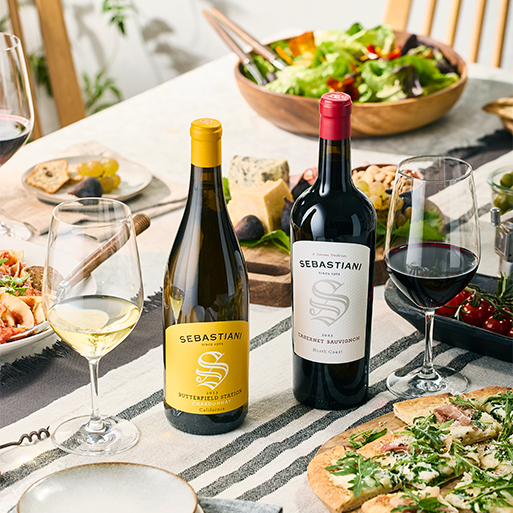 Two Sebastiani wine bottles on a table with fresh chopped salads, cheeses, pizza, and poured wine