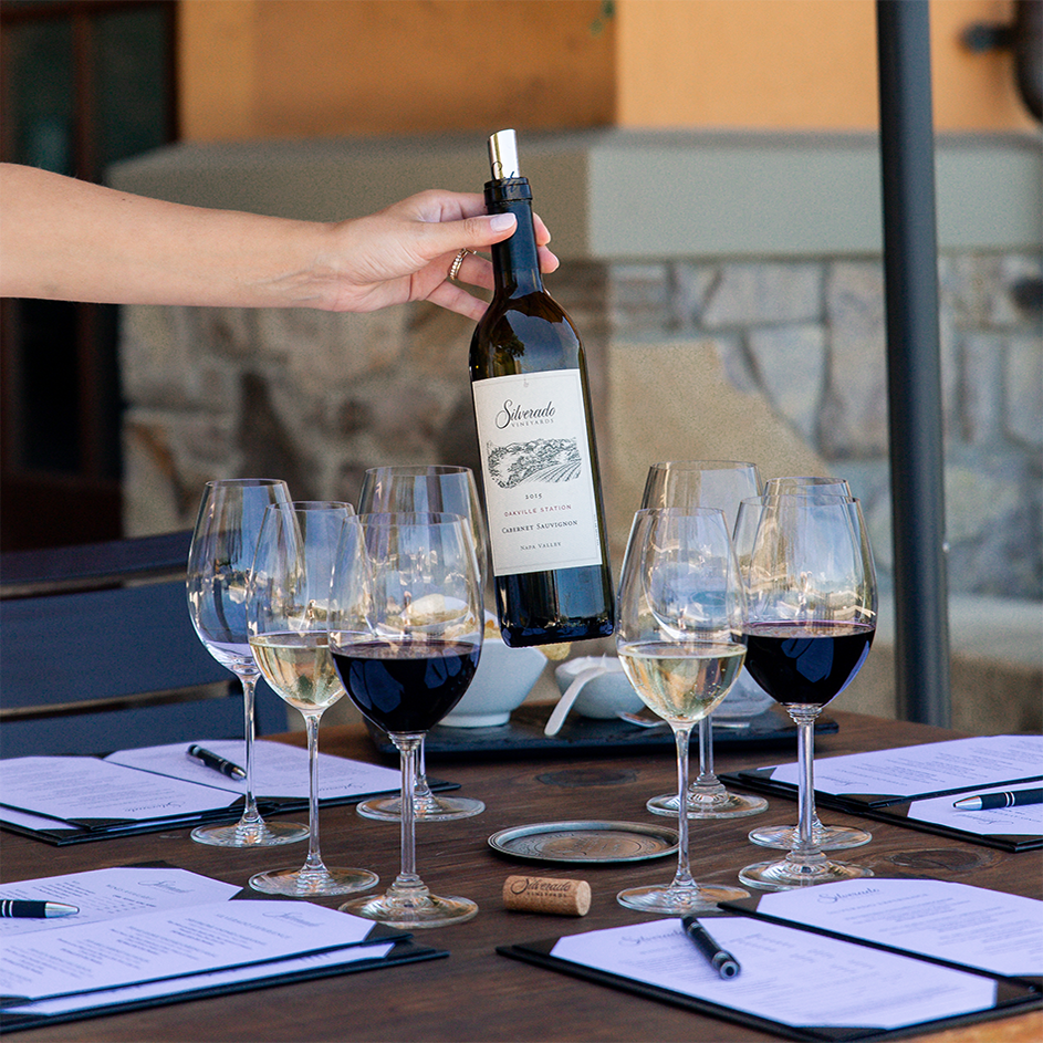 a table of menus and glasses of red silverado wine and a person holding a bottle of the wine