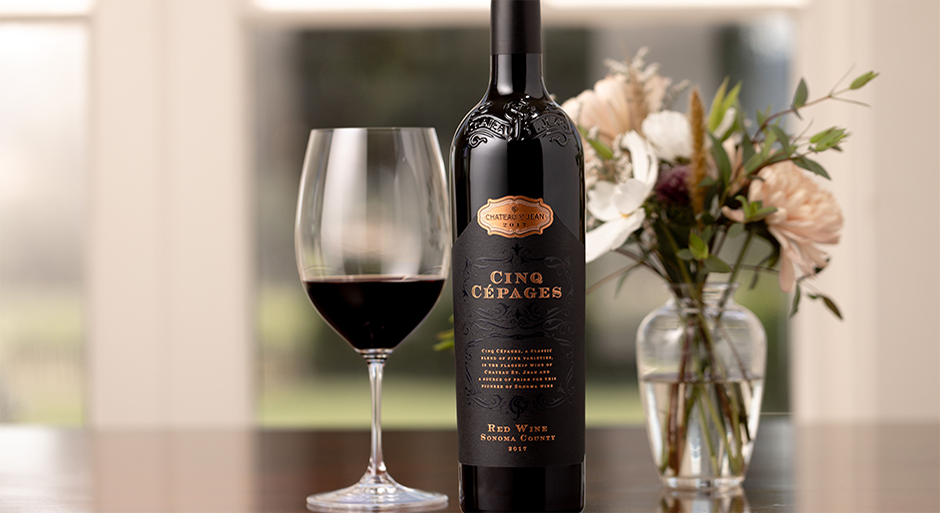 A bottle of Cinq Cépages wine next to a glass of wine and a bouquet of flowers