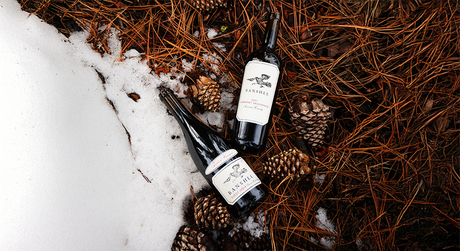 2 bottles of Banshee wines against a snowy background with pinecones