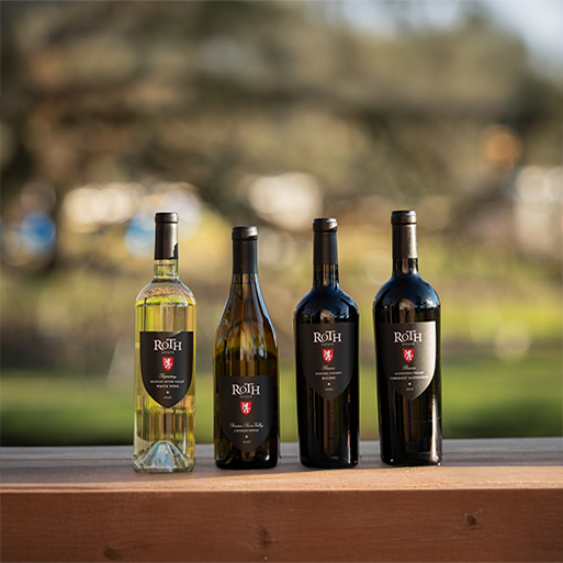 Four bottles of Roth wines on a ledge with soft focus vineyards in the background