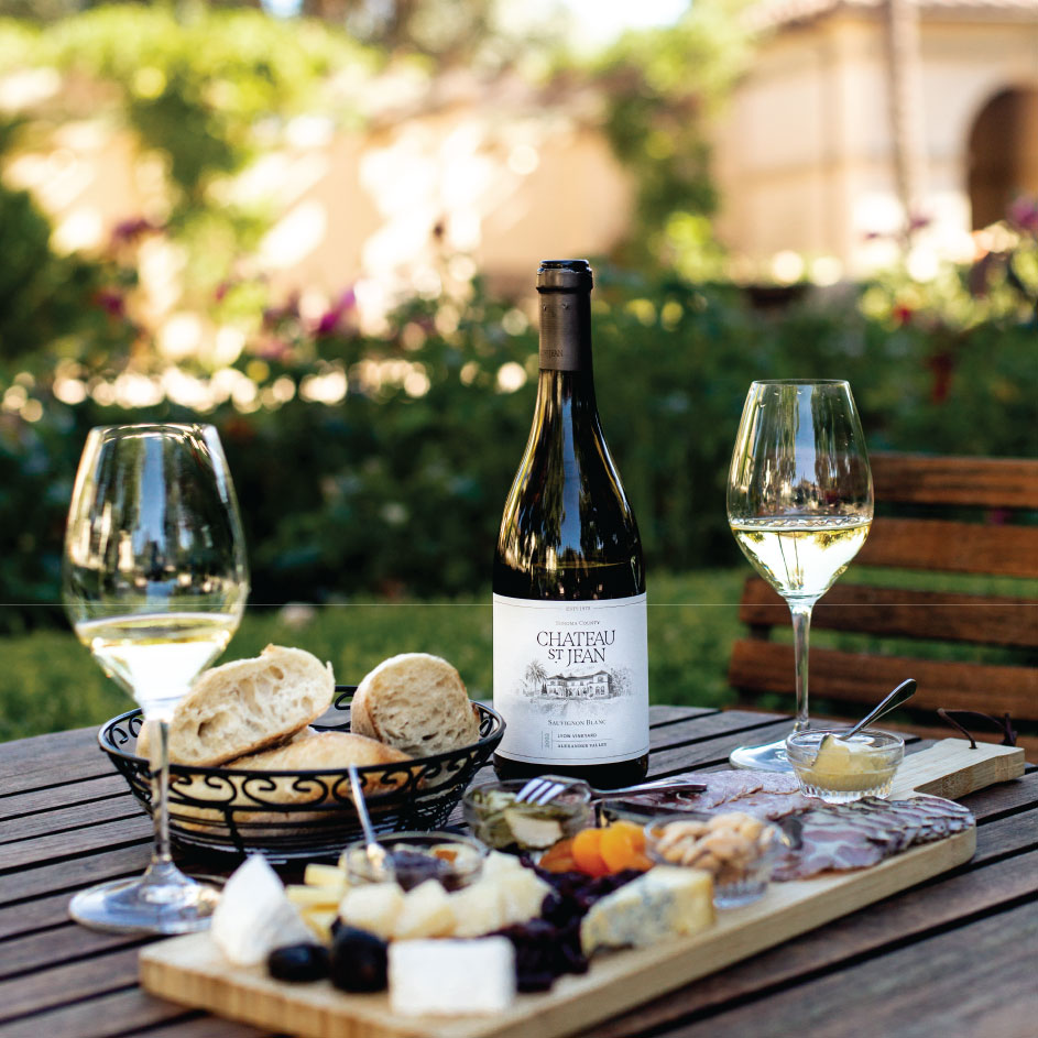 chateau st jean wine in a bottle and glasses on a table with a basket of bread and a charcuterie board