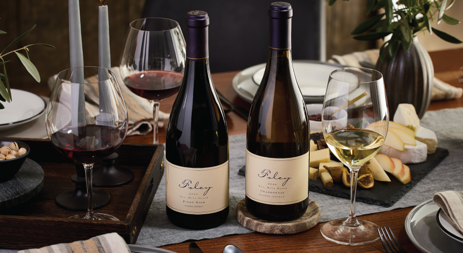 Foley Estates wine bottles with a glass of red and white wine on a table set with food, candles, flowers, and plates.