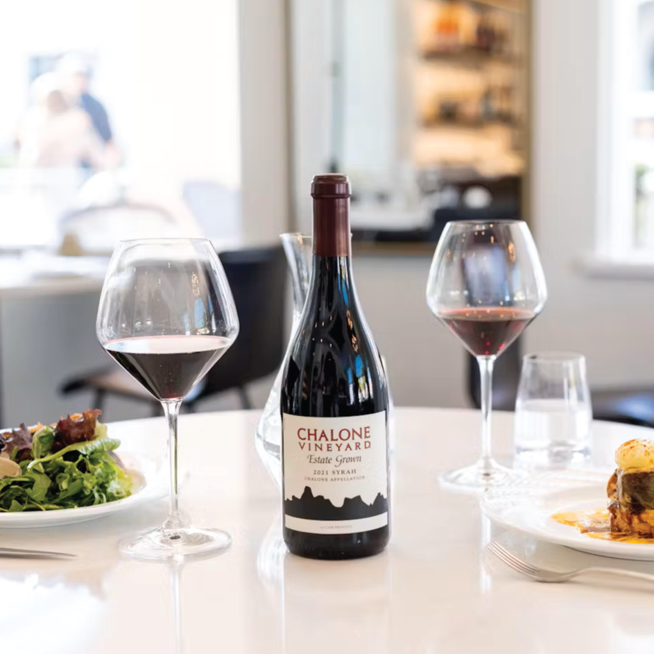 chalone wine bottled and in glasses on a table with plates of salad and burgers