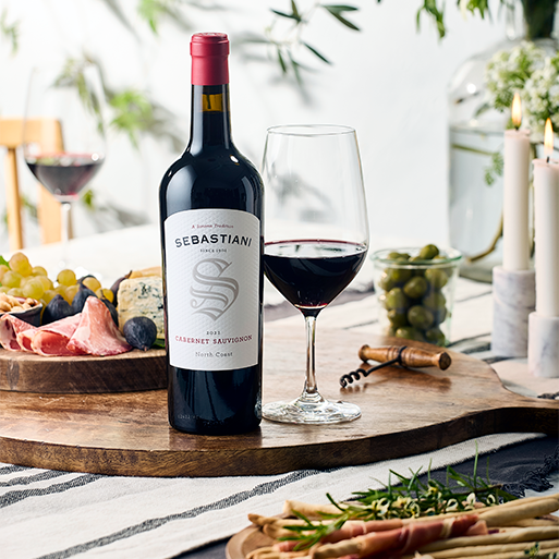 A bottle of Sebastiani wine with a poured glass on a table in a sunny outdoor setting with charcuterie