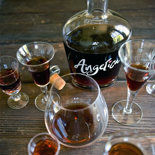 A bottle of Swansons Angelica Port with several poured glasses on a wooden table