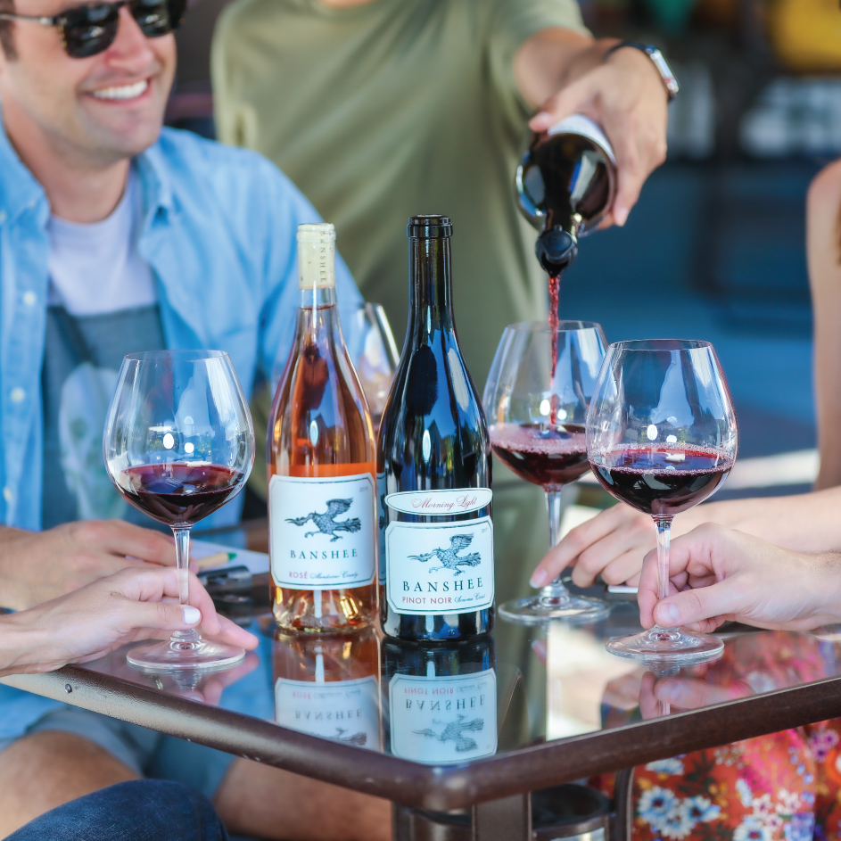 smiling people around a table of bottled and poured banshee wines