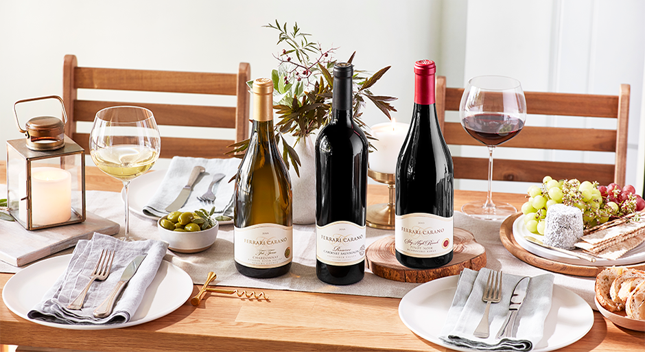 three bottls of ferrari carano wines on a table with nice settings, food, and glasses of wine